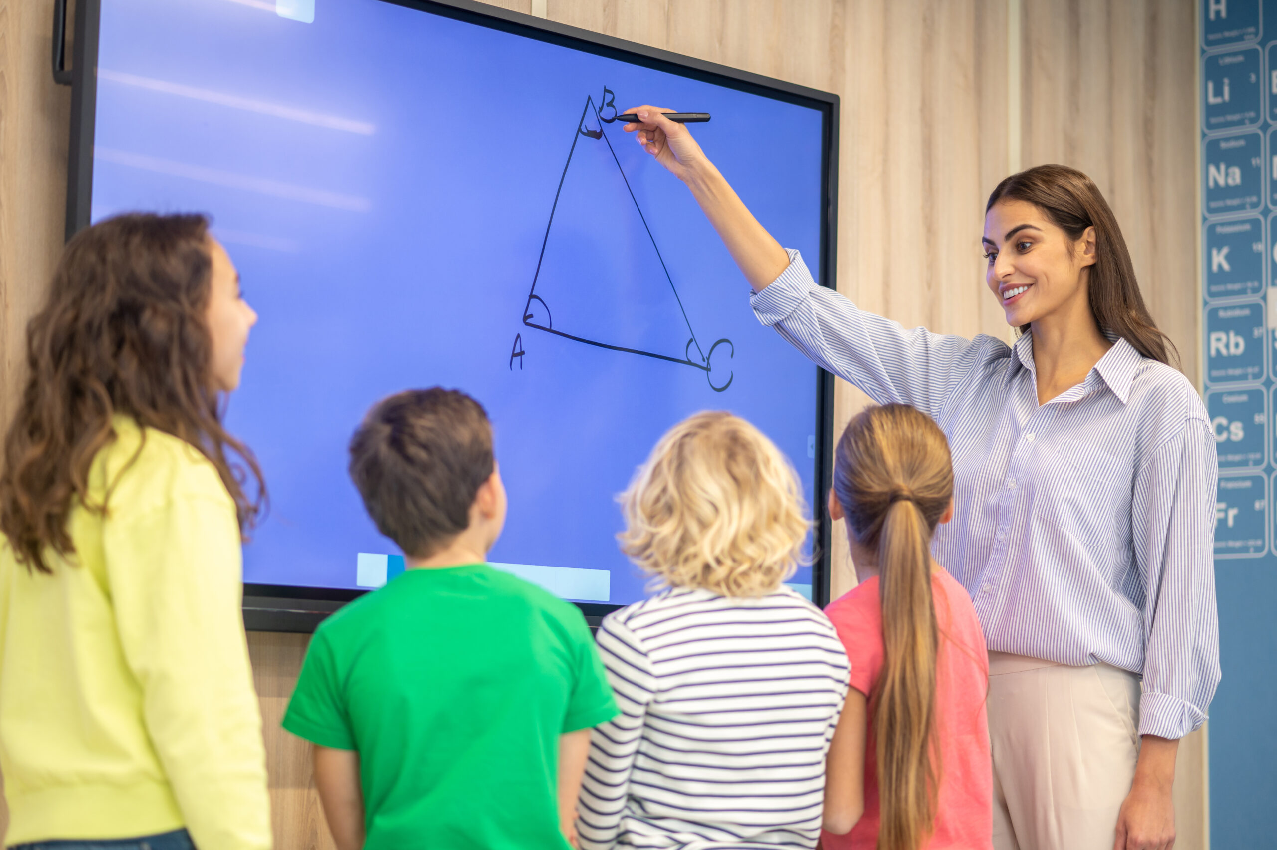 woman drawing showing triangle on blackboard to children